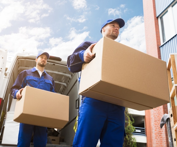 Two men moving boxes and furniture from a truck into an office building.